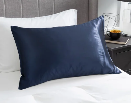 View of our Mulberry Silk Pillowcase in Navy resting on a white bed with a beige headboard.