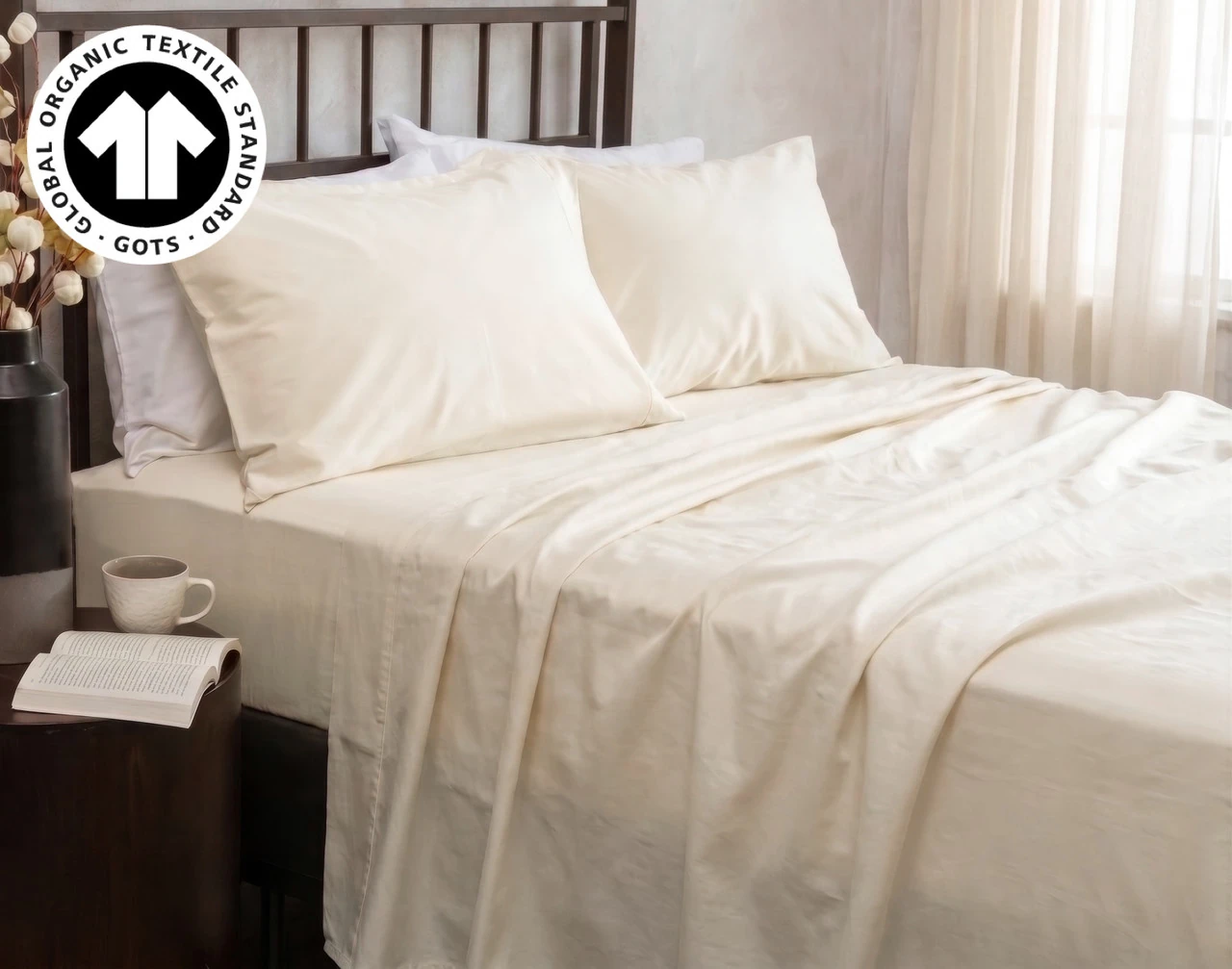 Our Undyed & Unbleached Organic Cotton Sateen Sheet Set dressed over a bed in a natural bedroom near a potted cotton plant.