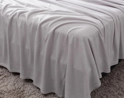 Angled view of a draped flat sheet over the corner of a bed fitted with our Cuddle Fleece Sheet Set in Granite.