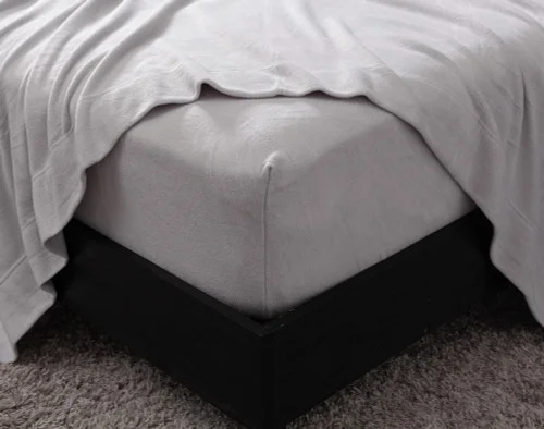 Close-up on the corner of our Cuddle Fleece Sheet Set in Granite with its fitted sheet wrapped around a queen mattress.