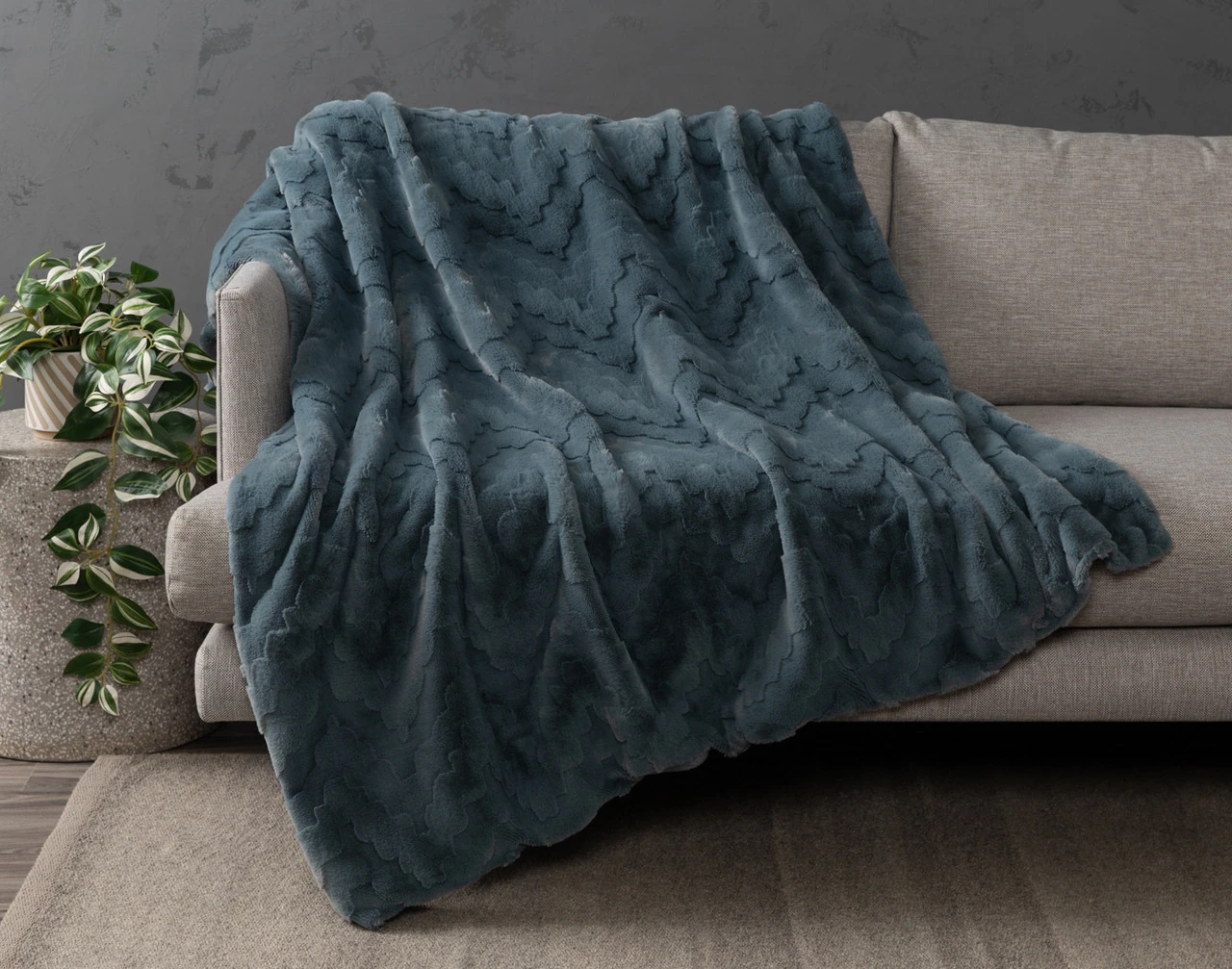 Our Teal Haze Geo Etched Throw draped over the left seat of a grey couch.