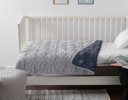 Side view of our Crib-Sized Stars Velvet Quilt draped over a small white crib.