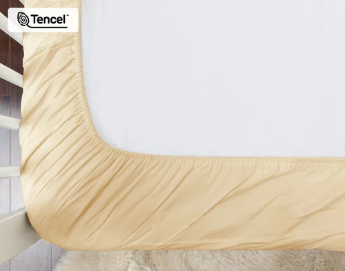 Underside of our Cornsilk BeechBliss TENCEL™ Modal Crib-Sized Fitted Sheet dressed over a small white crib mattress.