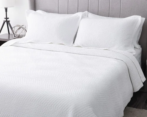 Angled view of our White Hermosa Quilt Set dressed over a plain queen bed.