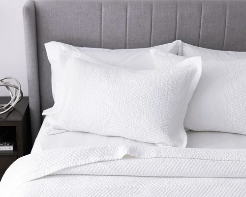 Pillow sham from our White Hermosa Quilt Set sitting against a headboard.