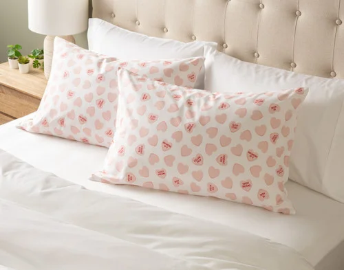 Our Pillow Talk Pillowcases - Candy Hearts at the head of a bed with white sheets.