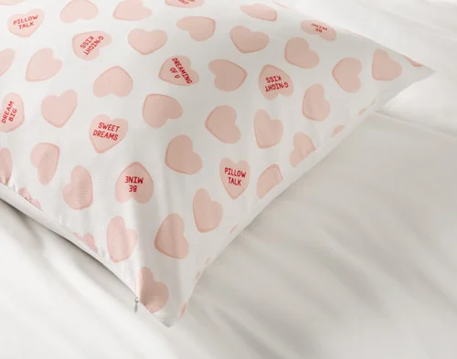 The corner of our Pillow Talk Pillowcase - Candy Hearts atop a white sheet.