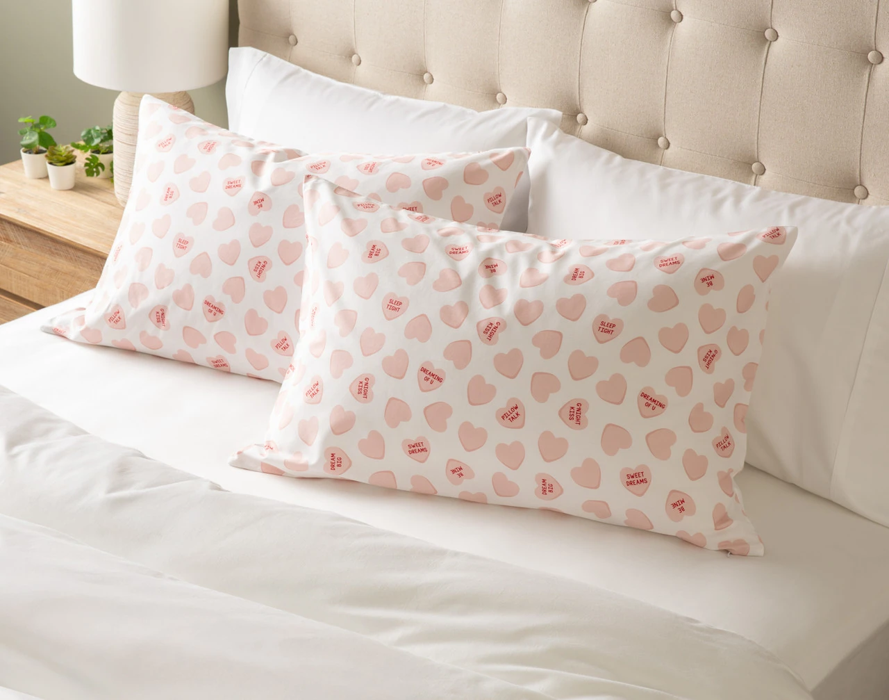 Our Pillow Talk Pillowcases - Candy Hearts at the head of a bed with white sheets.