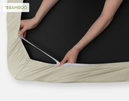 Our Bamboo Cotton Fitted Sheet in Thyme being fit over the corner of a mattress with its Stay Snug elastic.