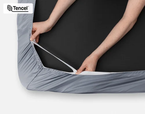 Close-up on two hands stretching the elastic snug fit band on the corner of our Eucalyptus Luxe TENCEL™ Lyocell Fitted Sheet in Cliffside.