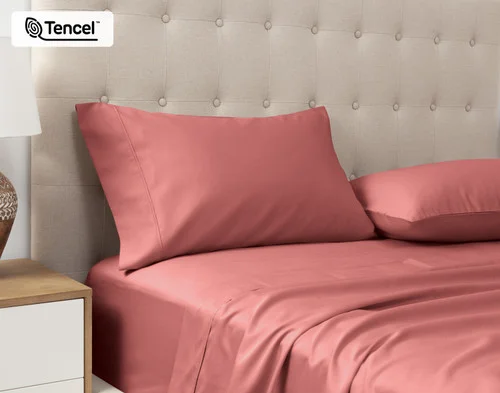 Angled view of our Eucalyptus Luxe TENCEL™ Lyocell Pillowcases in Raspberry Ice sitting against a headboard of a beige queen bed.