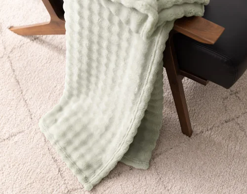 Angled view of our Sage Bubble Breeze Throw draped over a chair touching the floor.