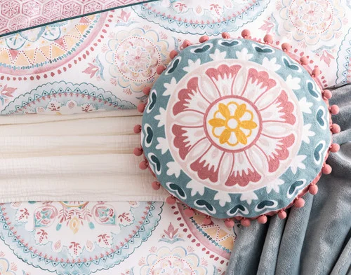 Our Mandira Round Cushion decorating a bed with our Mandira collection.