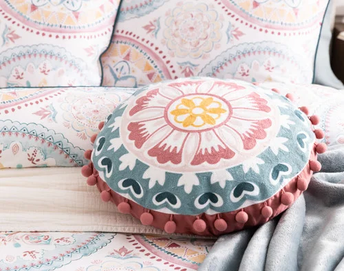 Our Mandira Round Cushion decorating a bed with our Mandira collection.