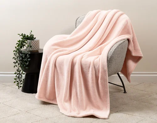 Our Velvet Plush Throw in Rosewater draped over a beige chair in a white living room.