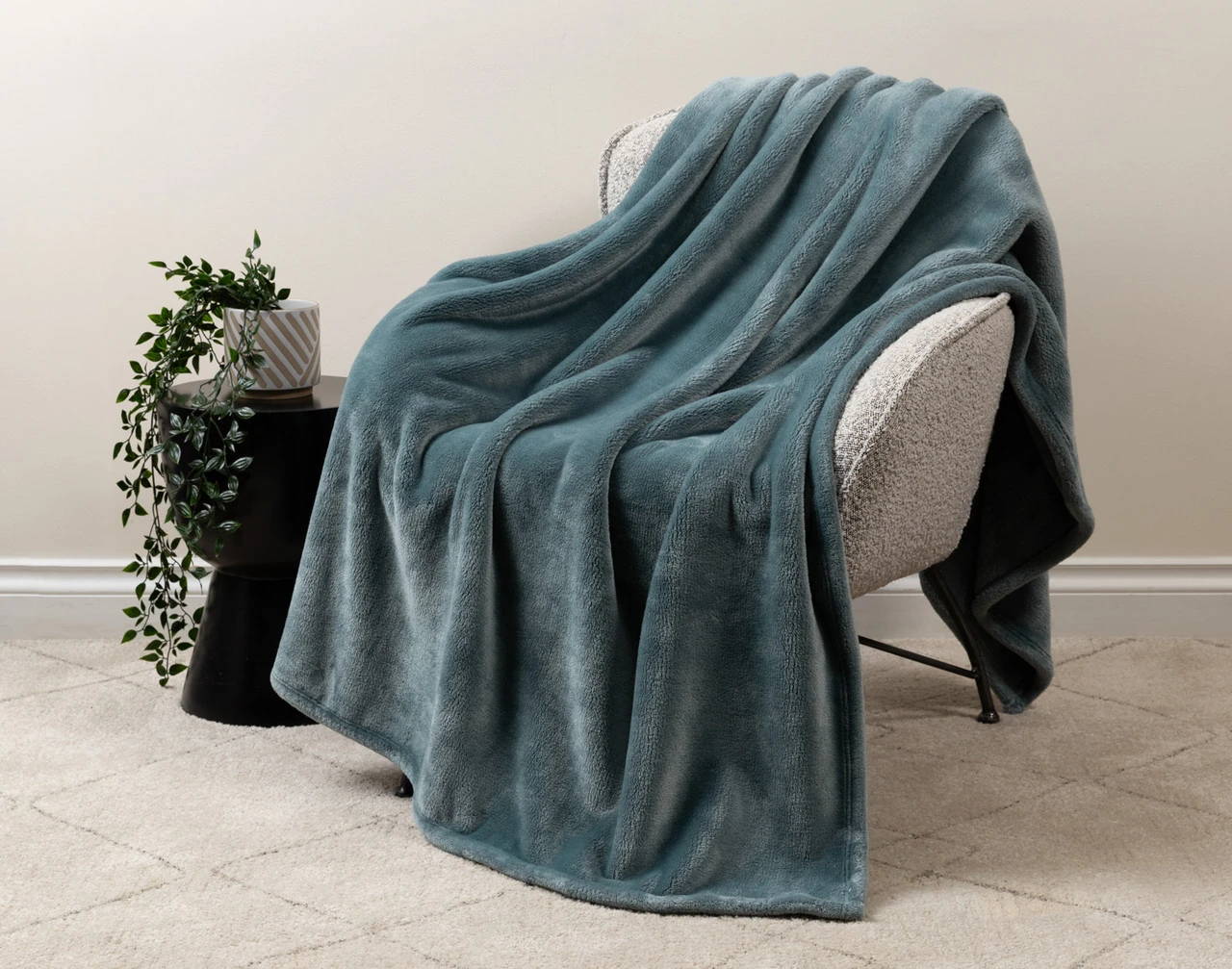 Our Velvet Plush Throw in Bluegrass draped over a beige chair in a white living room.