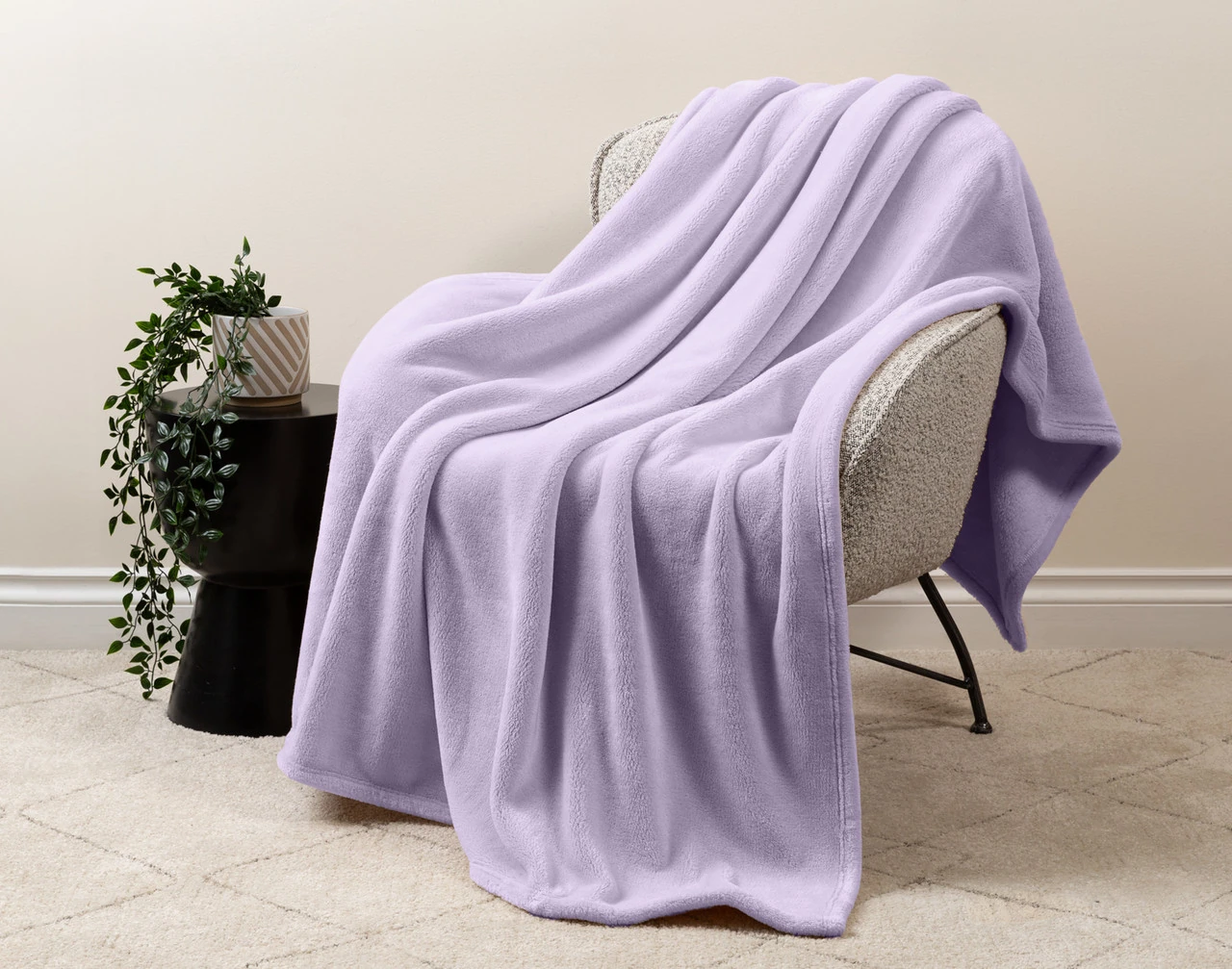 Our Velvet Plush Throw in Iris draped over a beige chair in a white living room.