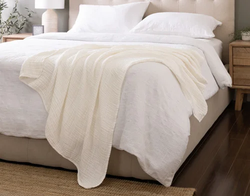 Our Bamboo Gauze Throw in White draped over the corner of a bed.