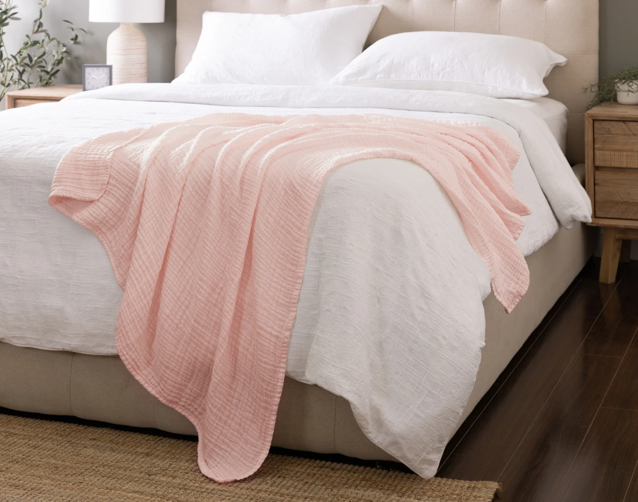 Our Bamboo Gauze Throw in Blossom draped over the corner of a bed.
