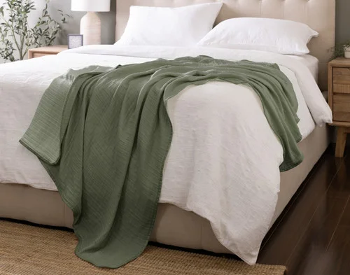 Our Bamboo Gauze Throw in Leaf draped over the corner of a bed.