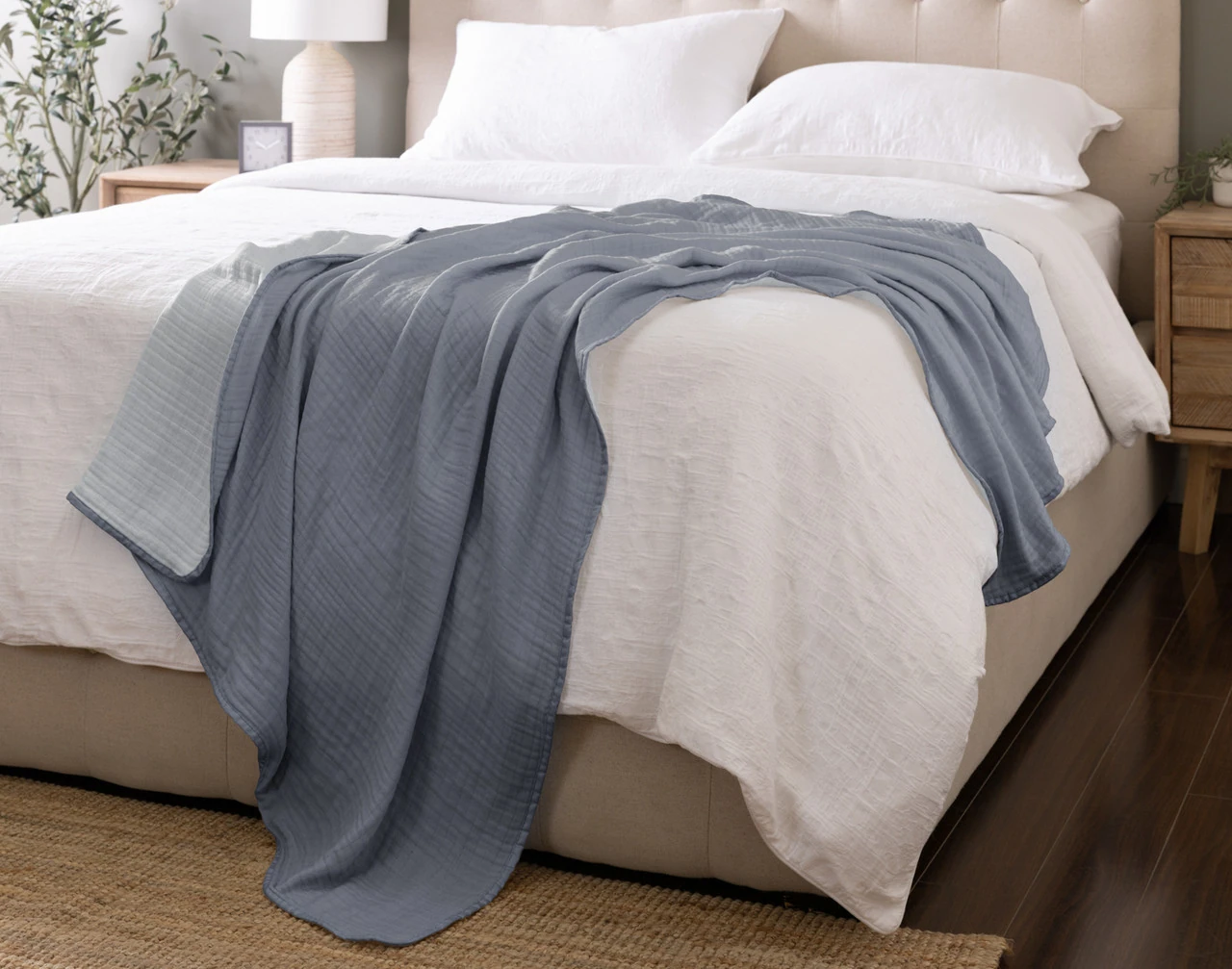 Our Bamboo Gauze Throw in Seaside draped over the corner of a bed.