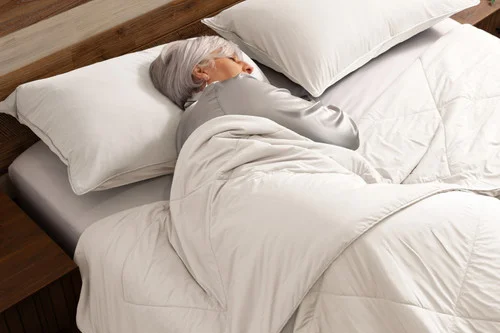 Woman sleeping on a bed with our Cloudstone Cool Touch Blanket and Pillowcases.