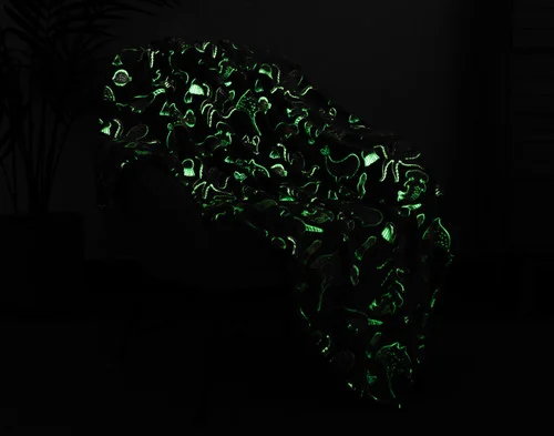 Dark view of our Under the Sea Glow In The Dark Throw draped over a chair with its design glowing green.