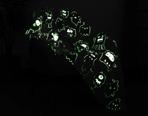 Dark view of our Snuggle Monsters Glow In The Dark Throw draped over a chair with its design glowing green.