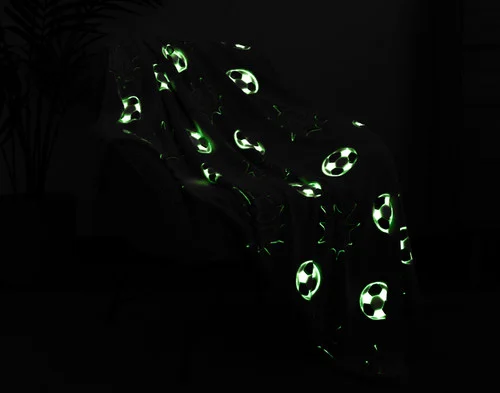 Dark view of our Kickoff Glow In The Dark Throw draped over a chair with its design glowing green.