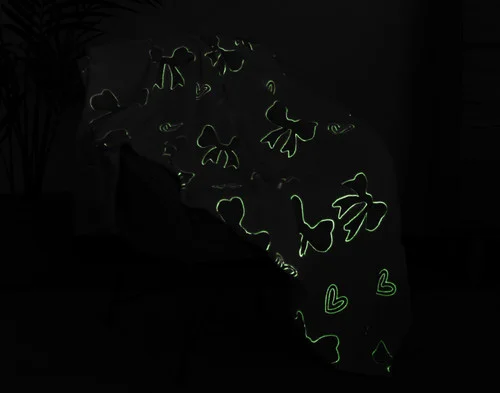 Dark view of our Bows & Hearts Glow In The Dark Throw draped over a chair with its design glowing green.