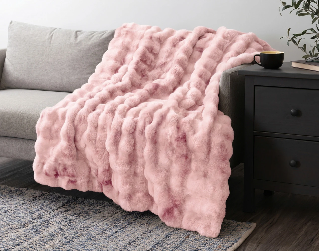 Our Bubble Faux Fur Throw in Peony draped over a grey couch.