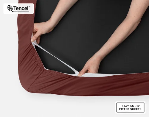 Bottom side of our BeechBliss TENCEL™ Modal Fitted Sheet in Mahogany with two hands showing the Snug Fit elastics holding it tightly on the mattress.