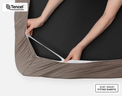 Bottom side of our BeechBliss TENCEL™ Modal Fitted Sheet in Bark with two hands showing the Snug Fit elastics holding it tightly on the mattress.