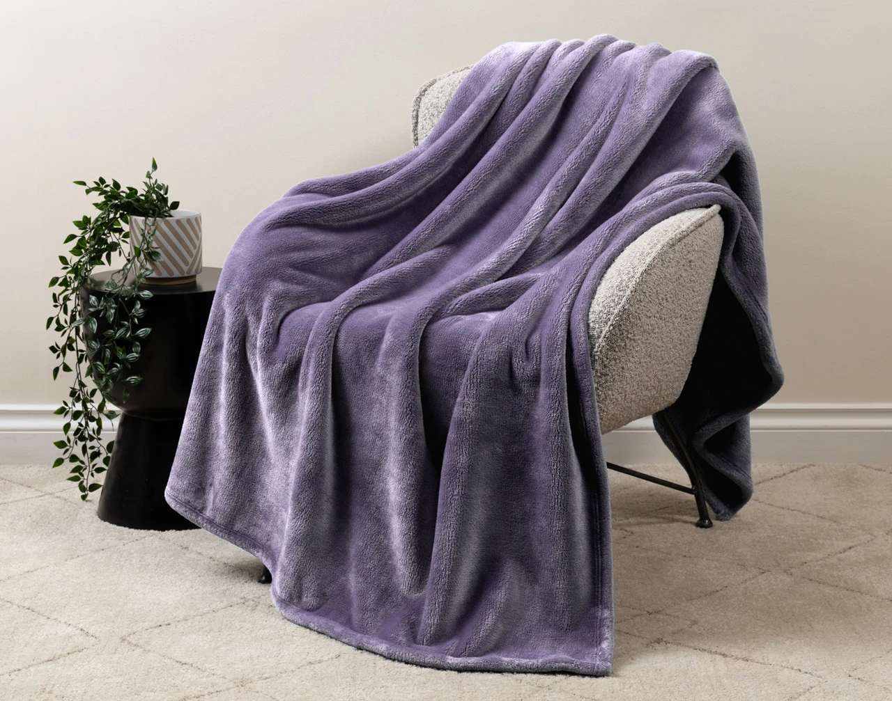 Our Velvet Plush Throw in Violet Smoke draped over a beige chair in a white living room.