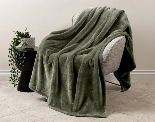 Our Velvet Plush Throw in Olive draped over a beige chair in a white living room.