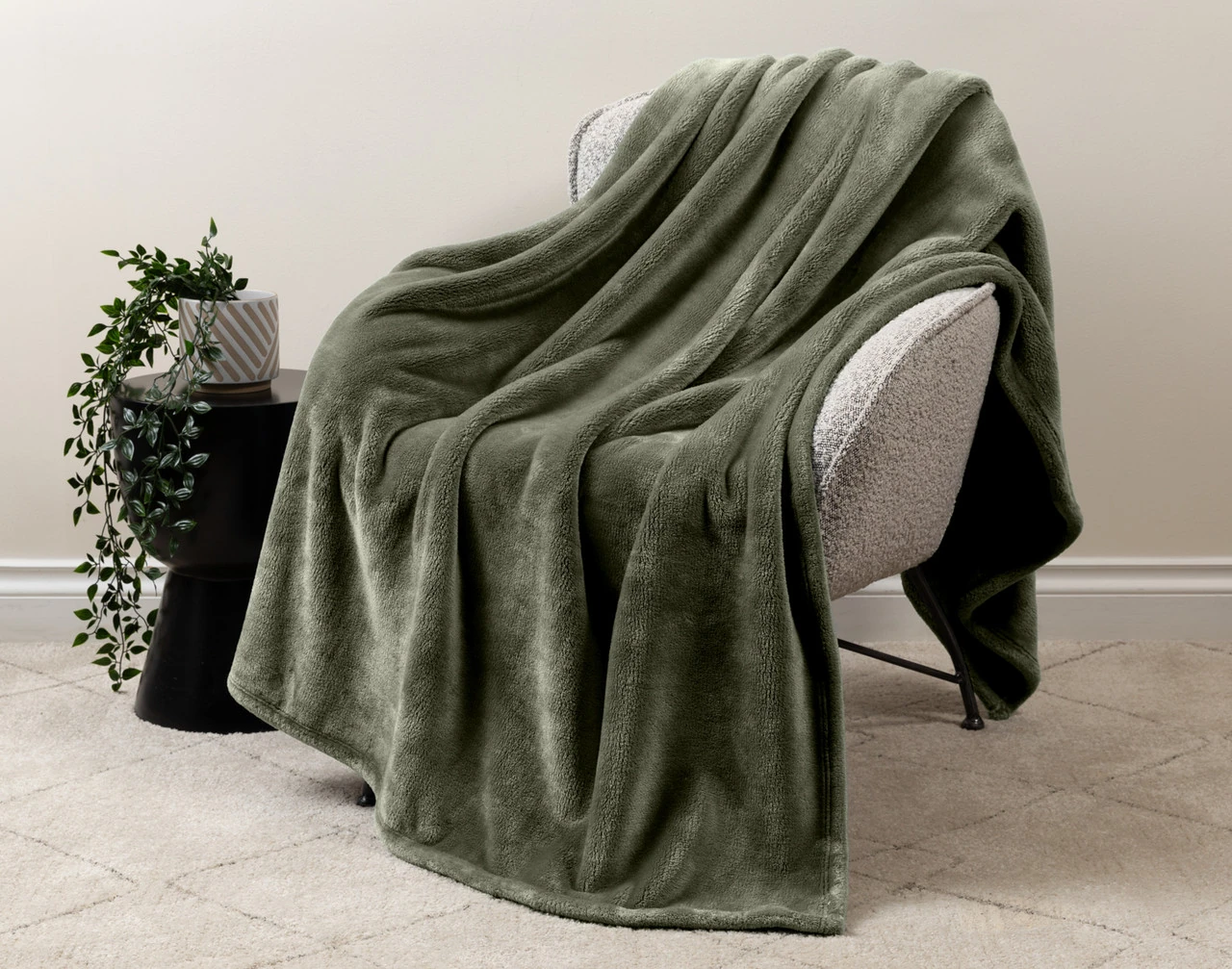 Our Velvet Plush Throw in Olive draped over a beige chair in a white living room.