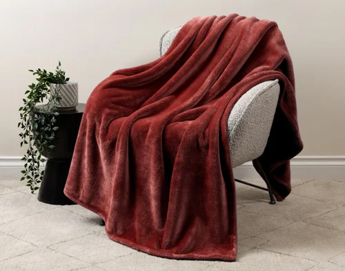 Our Velvet Plush Throw in Redwood draped over a beige chair in a white living room.