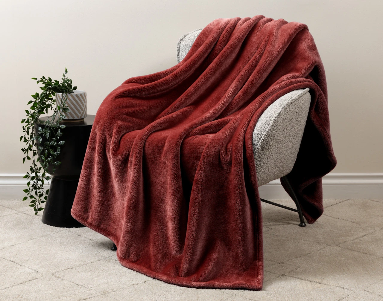 Our Velvet Plush Throw in Redwood draped over a beige chair in a white living room.