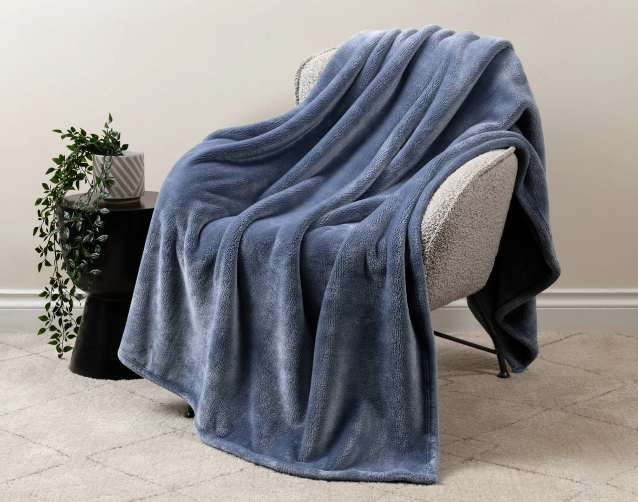 Our Velvet Plush Throw in Deep Wave draped over a beige chair in a white living room.