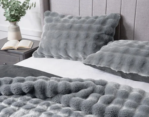 Angled view of our Granite Bubble Faux Fur Comforter Set to show its pillow shams leaning against a headboard.