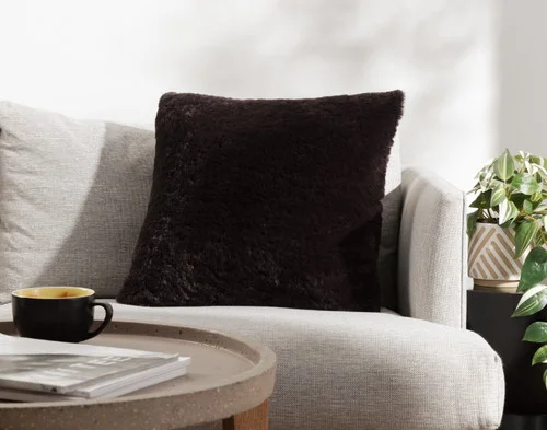 Angled view of our Espresso Poodle Faux Fur Square Cushion resting on a couch.
