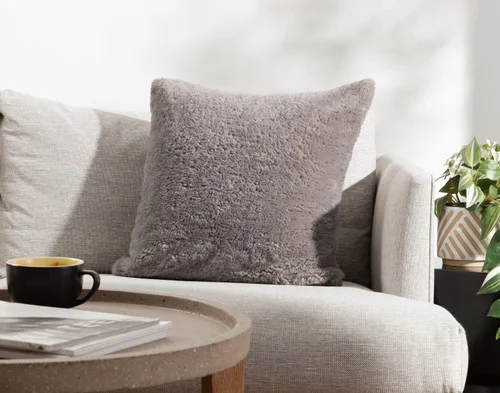 Angled view of our Ashwood Poodle Faux Fur Square Cushion resting on a couch.