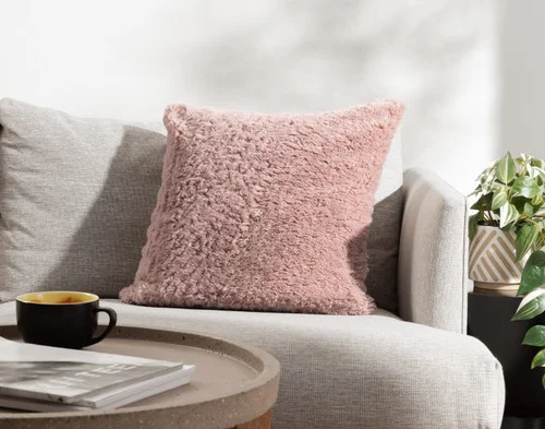 Angled view of our Dusty Rose Poodle Faux Fur Square Cushion resting on a couch.