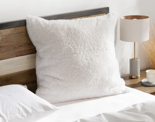 Angled view of our Ivory Poodle Faux Fur Euro Sham resting on a white bed.