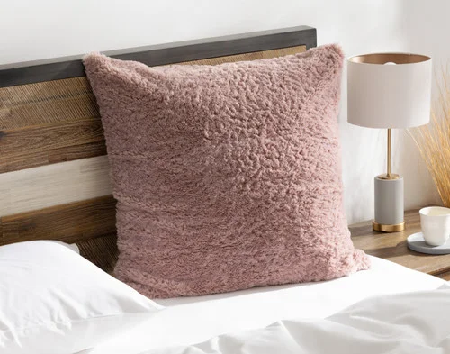 Angled view of our Dusty Rose Poodle Faux Fur Euro Sham resting on a white bed.