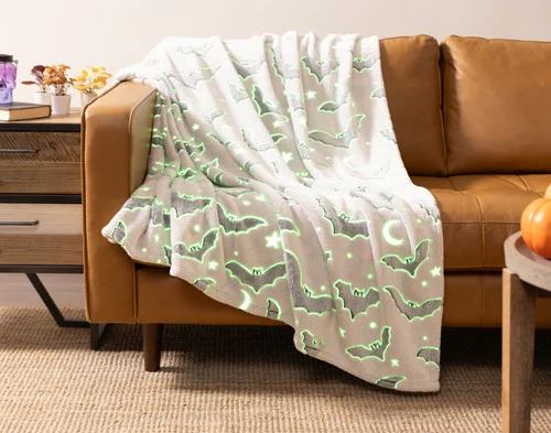 Our Midnight Bats Glow in the Dark Fleece Throw draped over a couch seat.