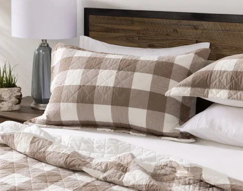 Angled view of the pillow shams for our Wellington Ash Cotton Quilt Set resting against the headboard of a white bed.