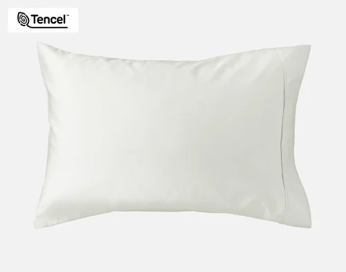 Angled view of our Eucalyptus Luxe Pillowcases in Oyster sitting against a headboard of a beige queen bed.