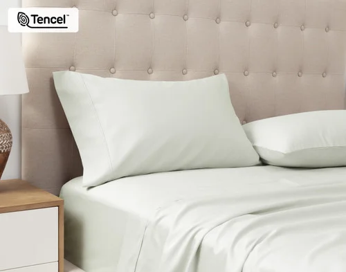 Angled view of our Eucalyptus Luxe Pillowcases in Oyster sitting against a headboard of a beige queen bed.