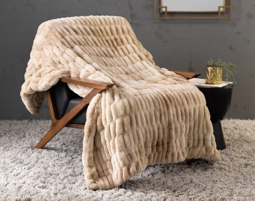 Our Cocoon Plush Throw in Caramel draped over a chair in a grey room.